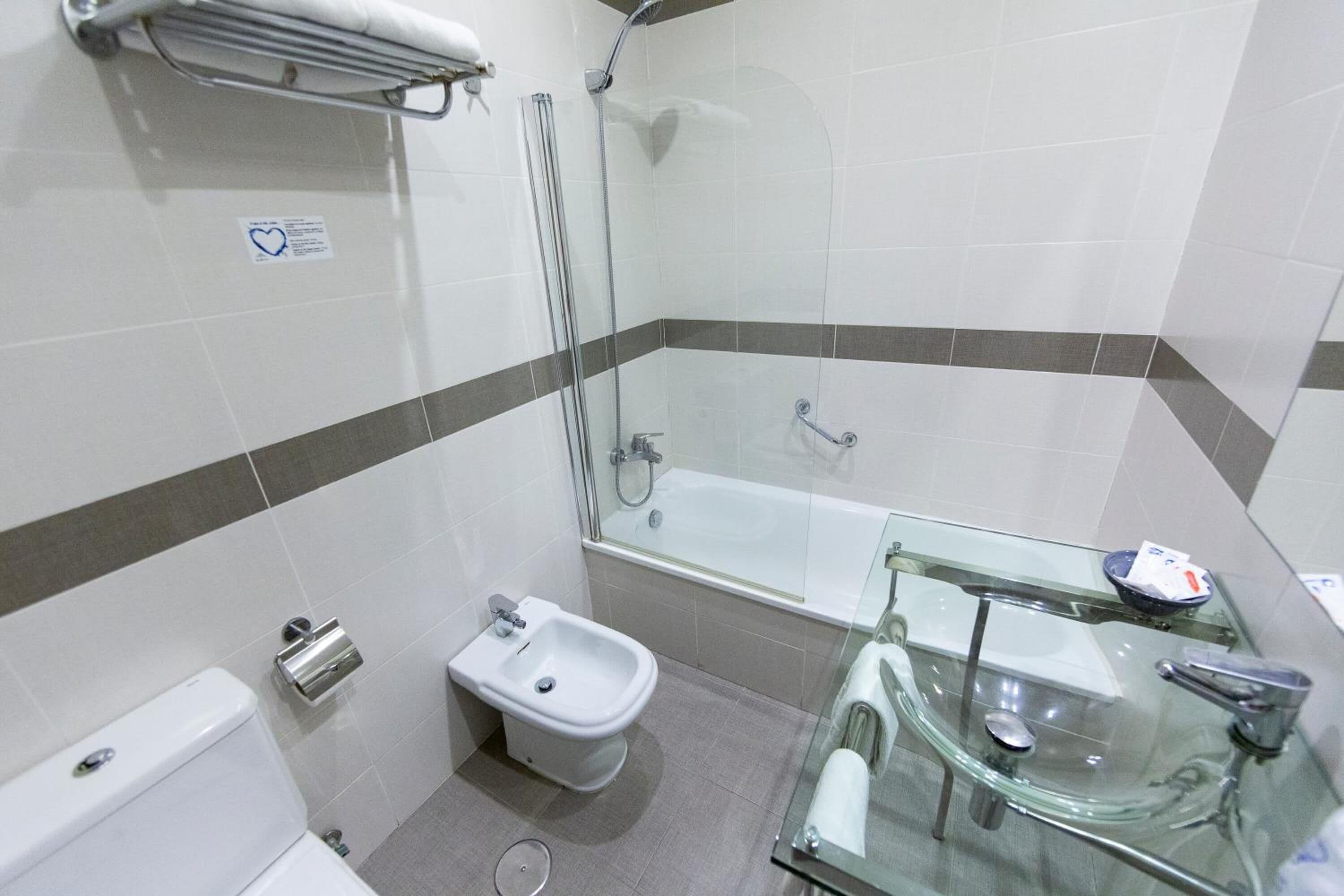 A modern bathroom with a glass shower enclosure, a glass sink, and a bidet.