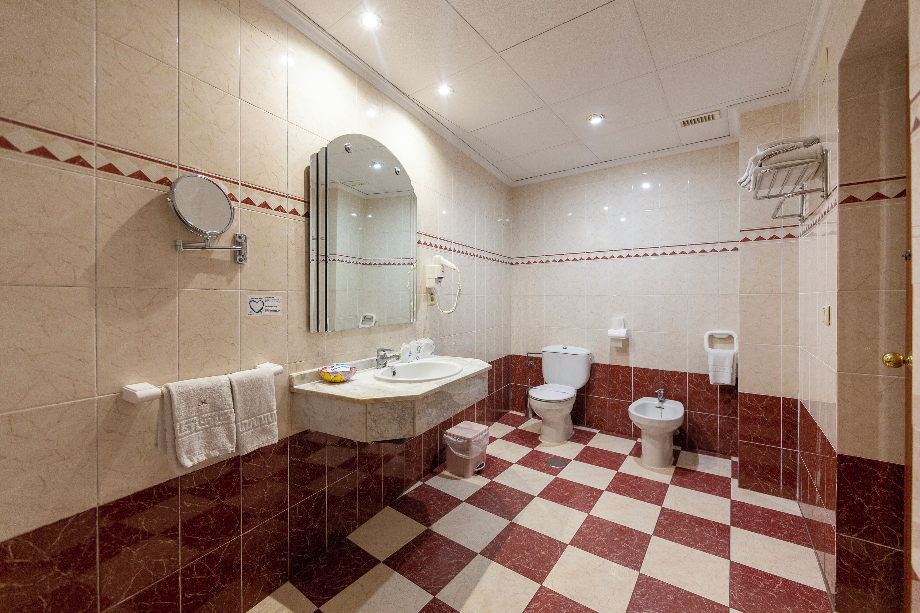 A bathroom with a checkered floor, a sink, a toilet, a bidet, and a mirror.