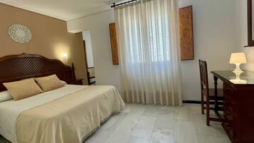A hotel room with a bed, a desk, a chair, and a window with curtains.