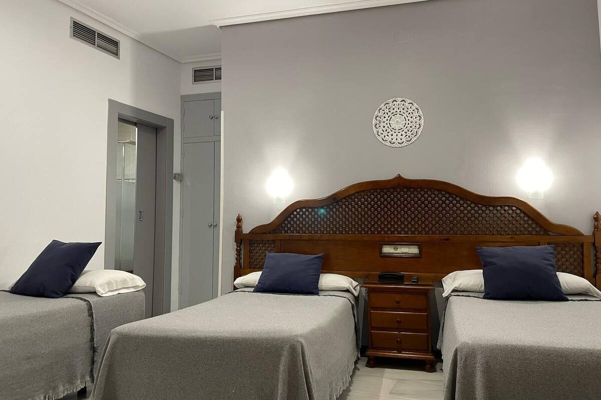 Una habitación con dos camas individuales, cabecera de madera, mesita de noche y lámpara de pared.