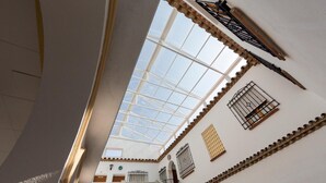 Un interior con techos altos, un tragaluz, paredes blancas con adornos decorativos y un balcón con barandilla.
