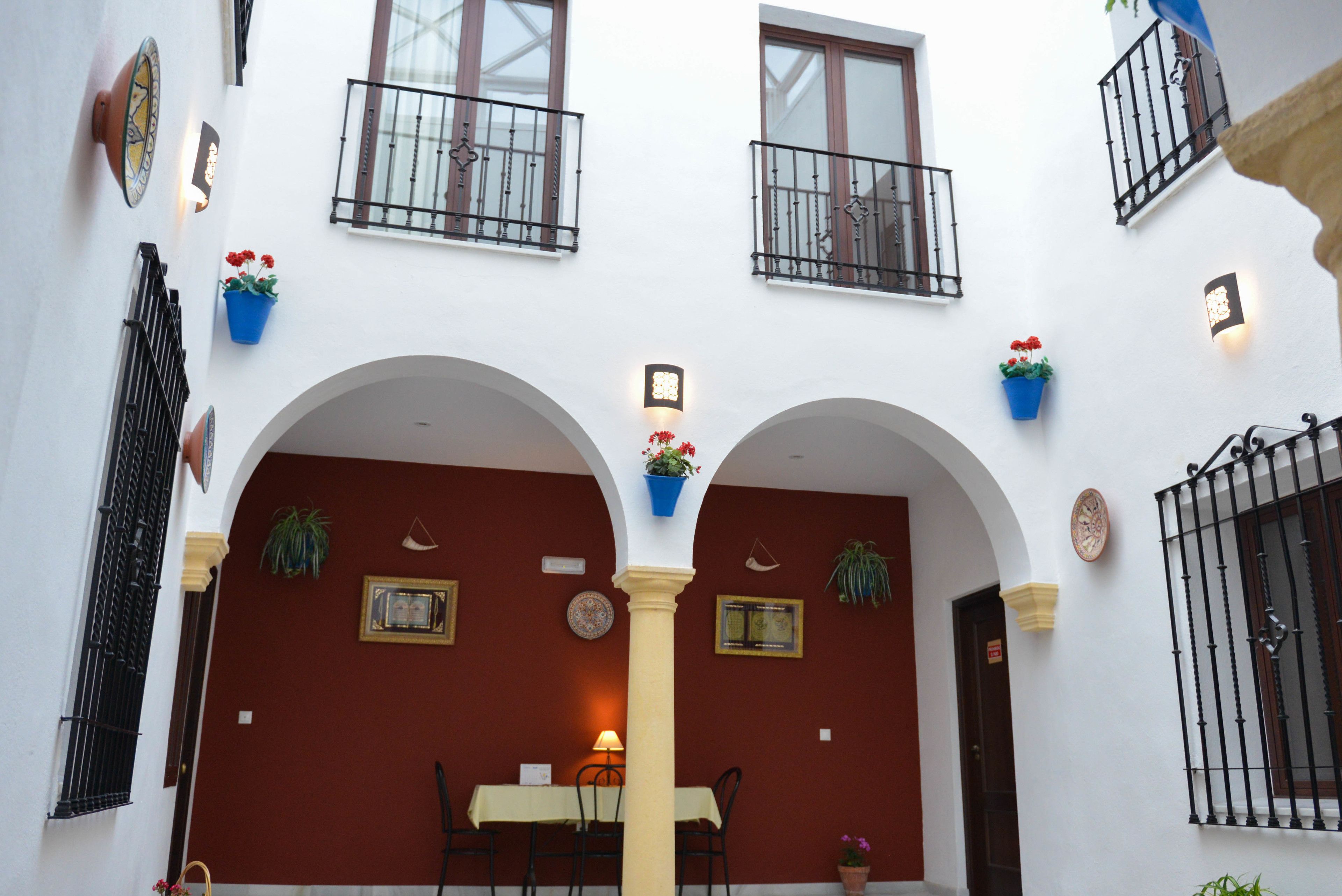 A courtyard with a central table and chairs, surrounded by arches and potted plants.