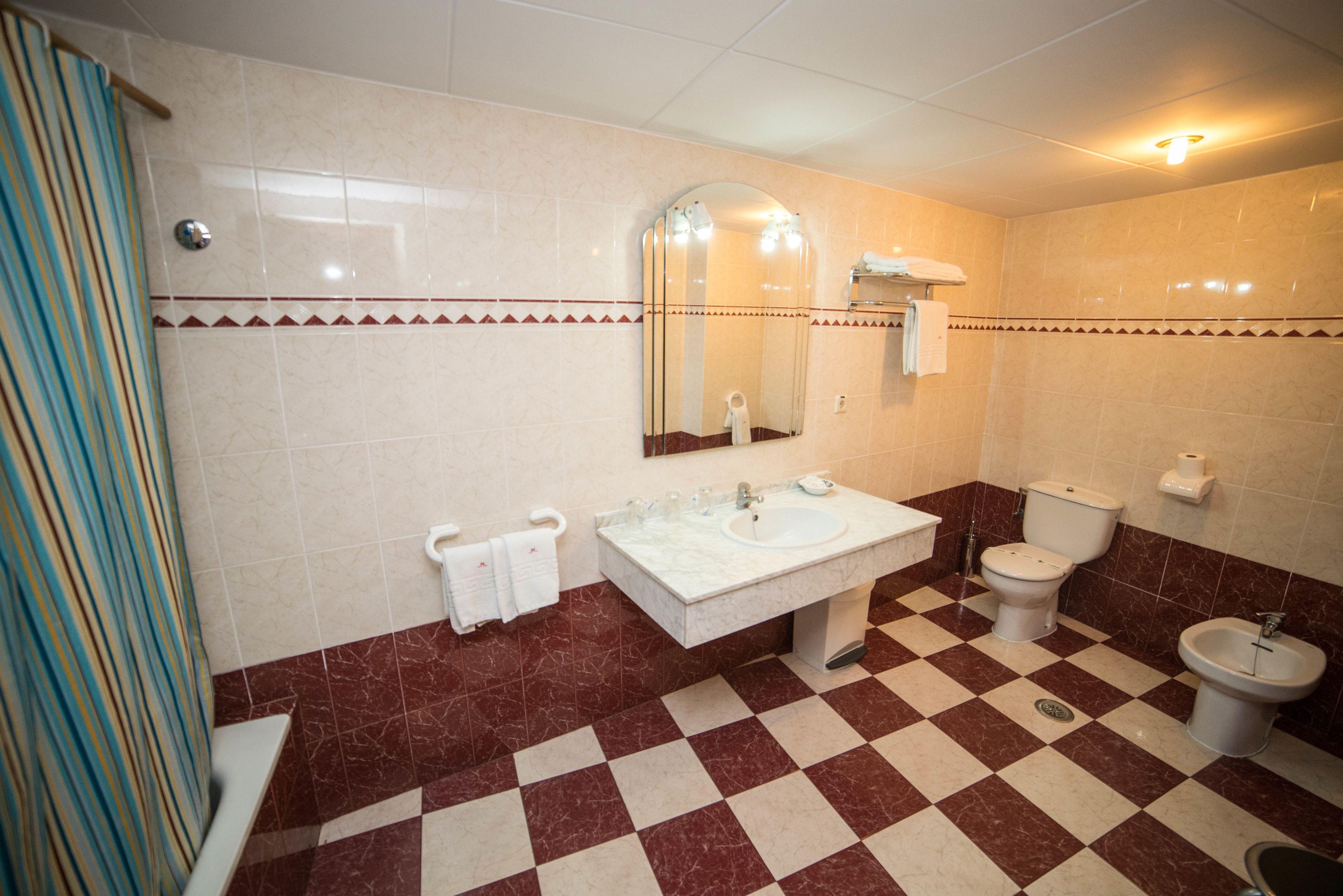 A bathroom with a checkered floor, a sink, a toilet, and a bidet.