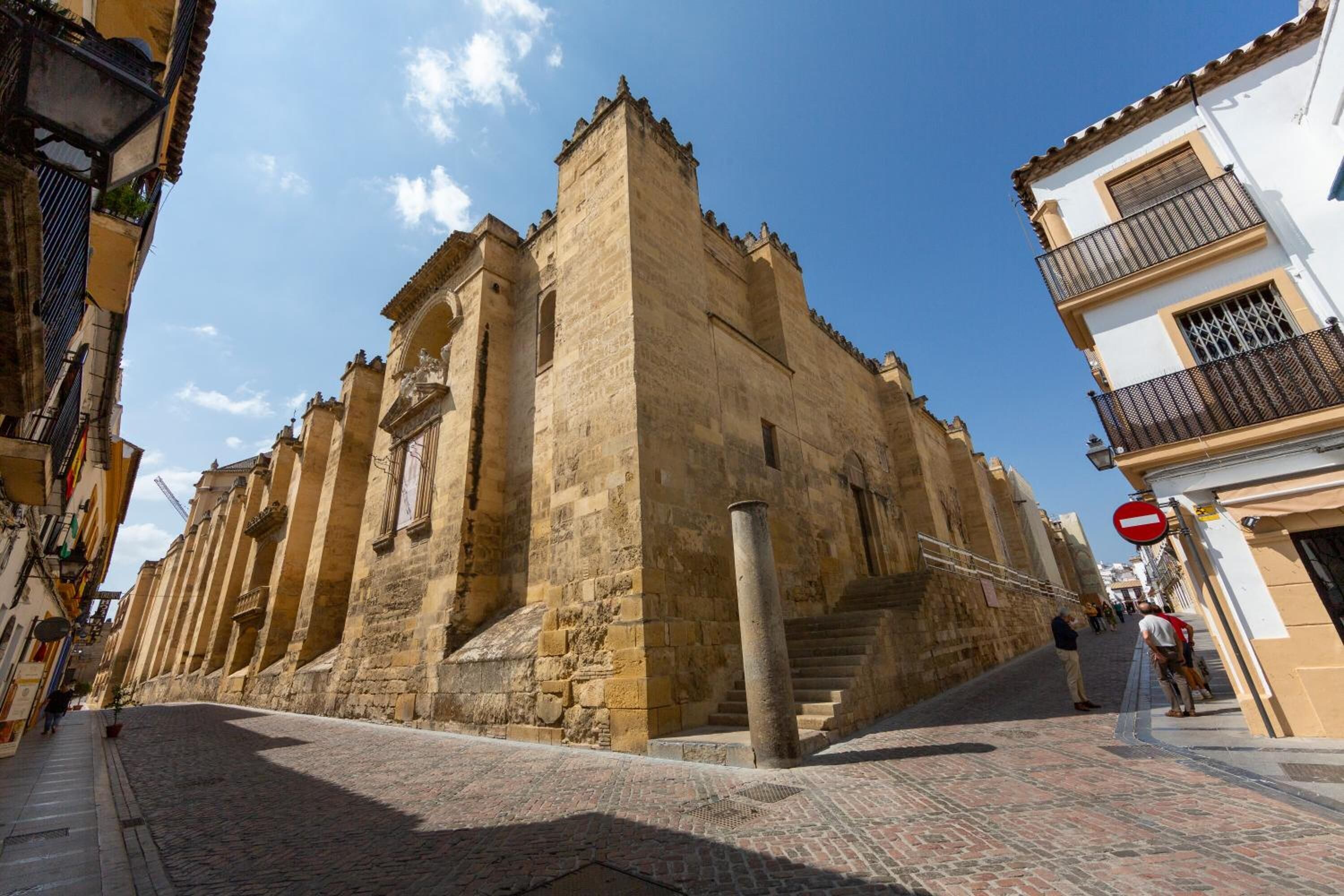 A historic stone building with a prominent tower, a cobblestone street, and a pedestrian walkway.