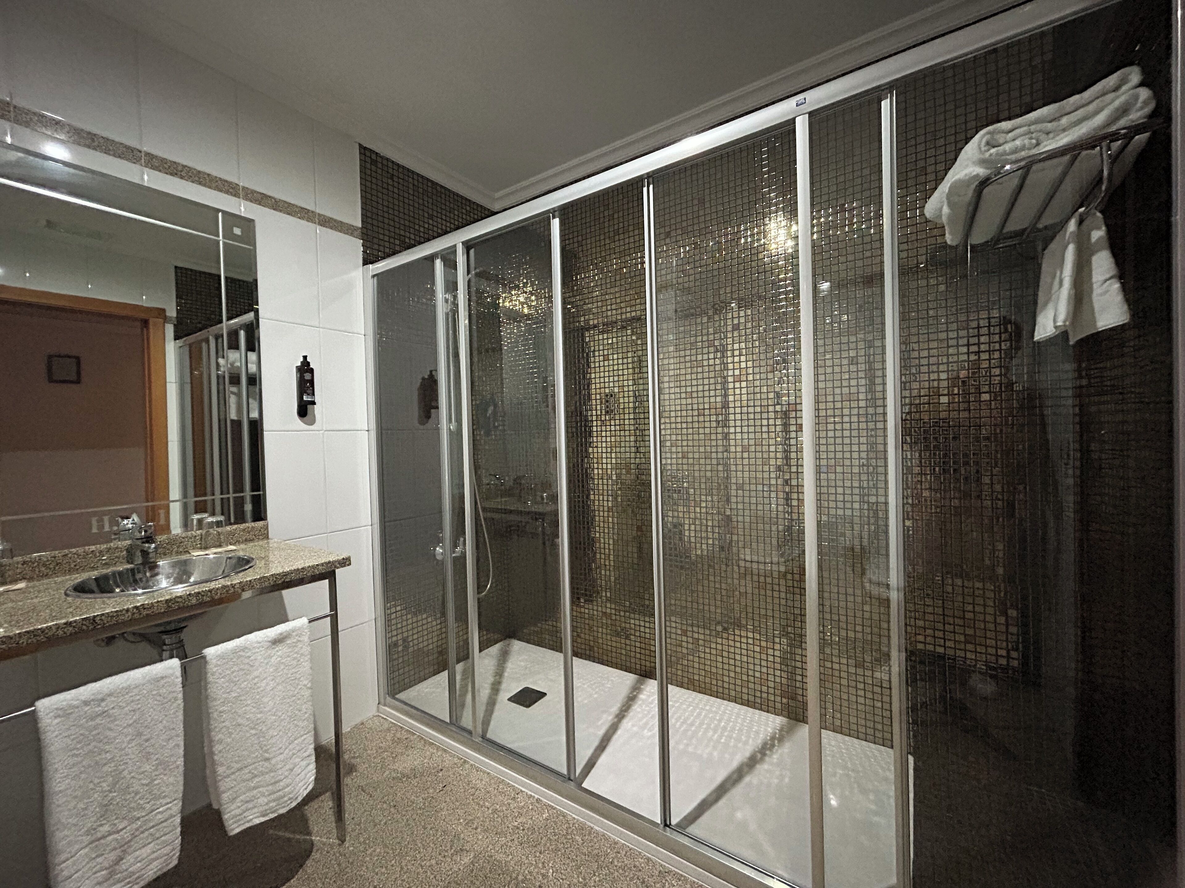 A modern bathroom with a glass-enclosed shower, a granite countertop, and a large mirror.