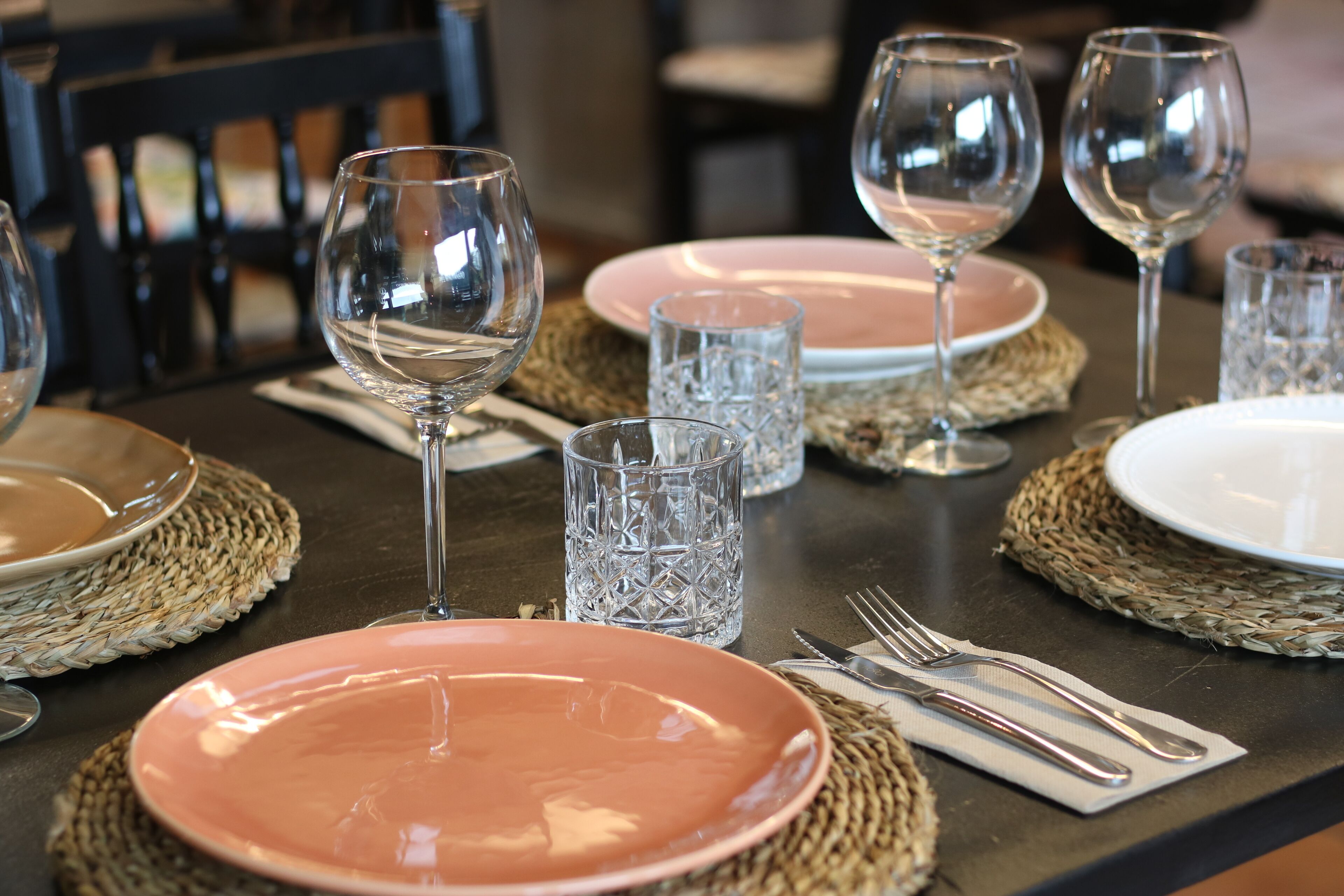 Una mesa dispuesta con platos, vasos y cubiertos, con individuales tejidos.