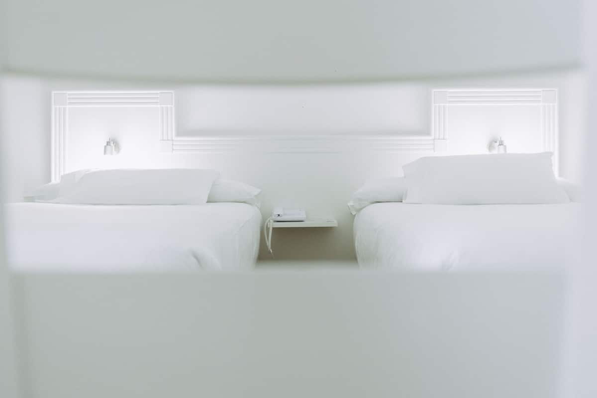 Habitación de hotel minimalista con dos camas, una mesita de noche y una ventana con persianas.