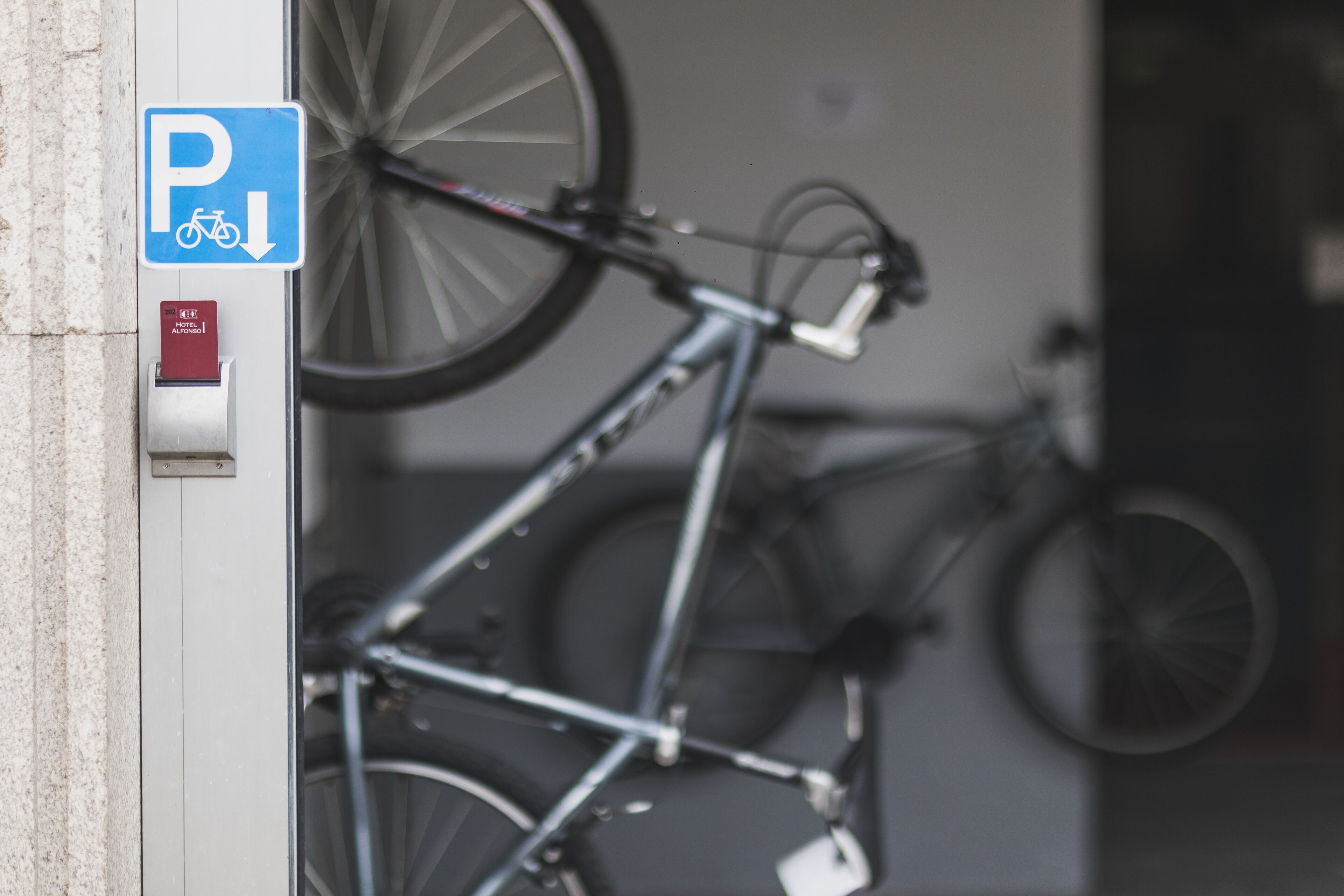 A bicycle parked in a designated bike rack area with a blue parking sign and a red ticket machine.