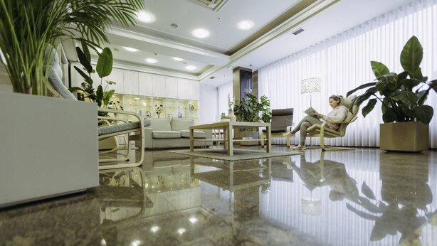 Een ruime lobby met een gepolijste marmeren vloer, een zithoek met een bank en fauteuils, en diverse potplanten.