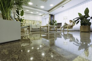 Un vestíbulo amplio con un suelo de mármol pulido, una zona de estar con sofá y sillones, y varias plantas en macetas.