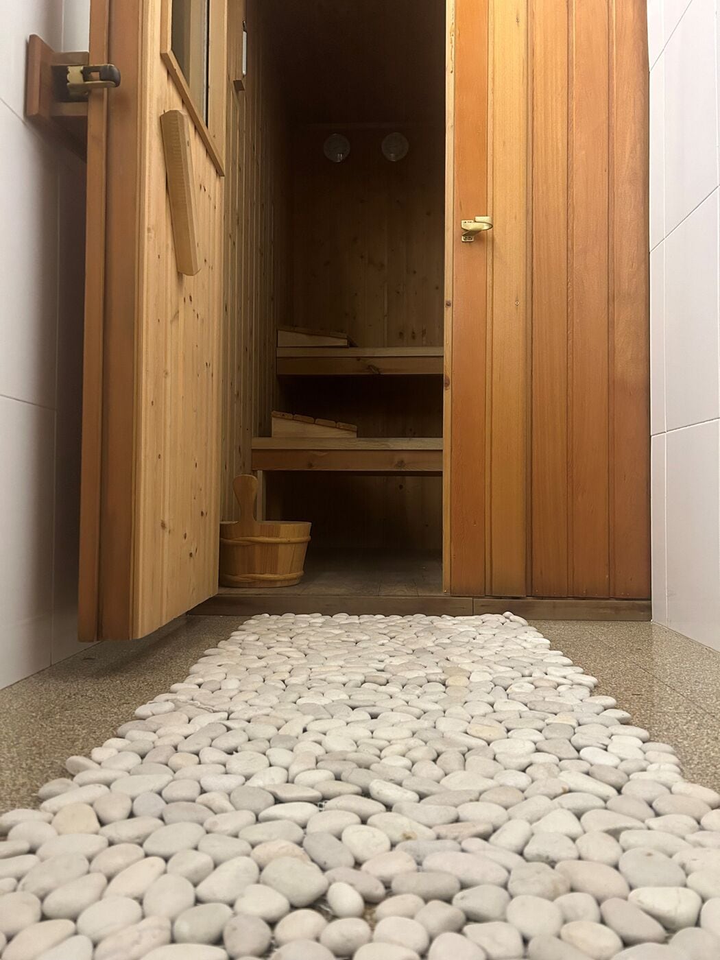 A wooden interior with a pebbled floor leading to a room with shelves and a wooden door.