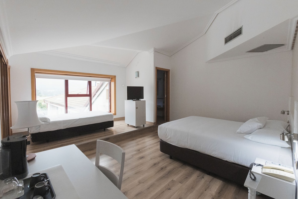 Una habitación de hotel moderna con una cama grande, un escritorio con lámpara, una silla y vistas al exterior.