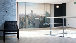 Een moderne kamer met een stadsgezicht muurschildering, een zwarte lederen fauteuil en een glazen hekwerk.