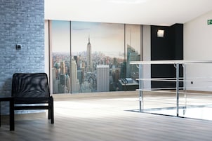 Una habitación moderna con un mural de paisaje urbano, un sillón de cuero negro y una barandilla de vidrio.