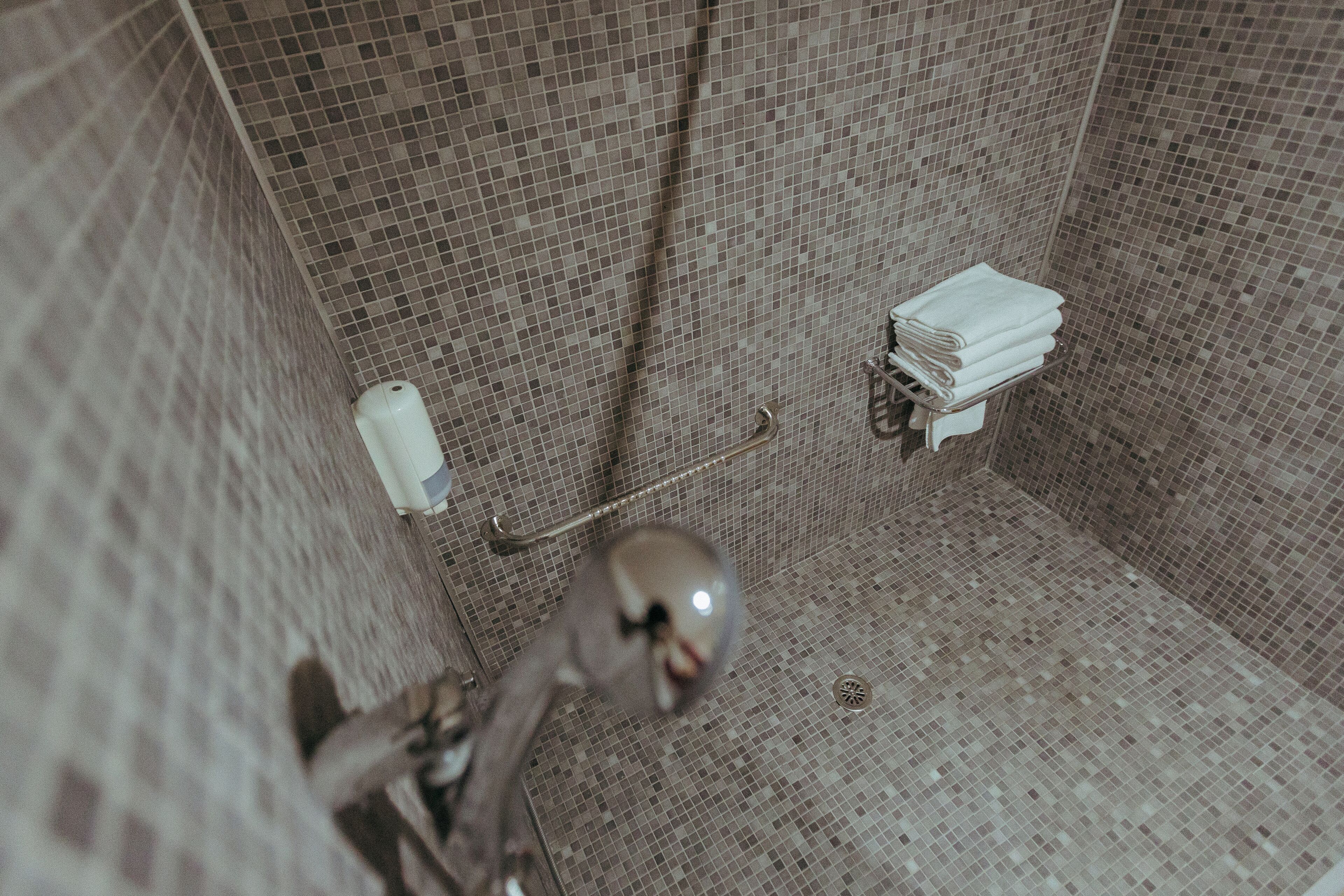 A tiled bathroom with a shower area, a toilet, and a towel rack.