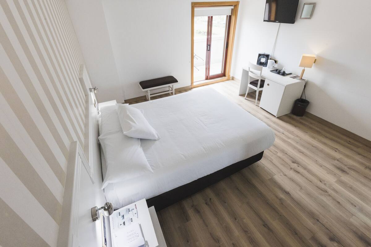 Habitación de hotel con una cama grande, un escritorio con silla, un televisor y ventana con vistas.