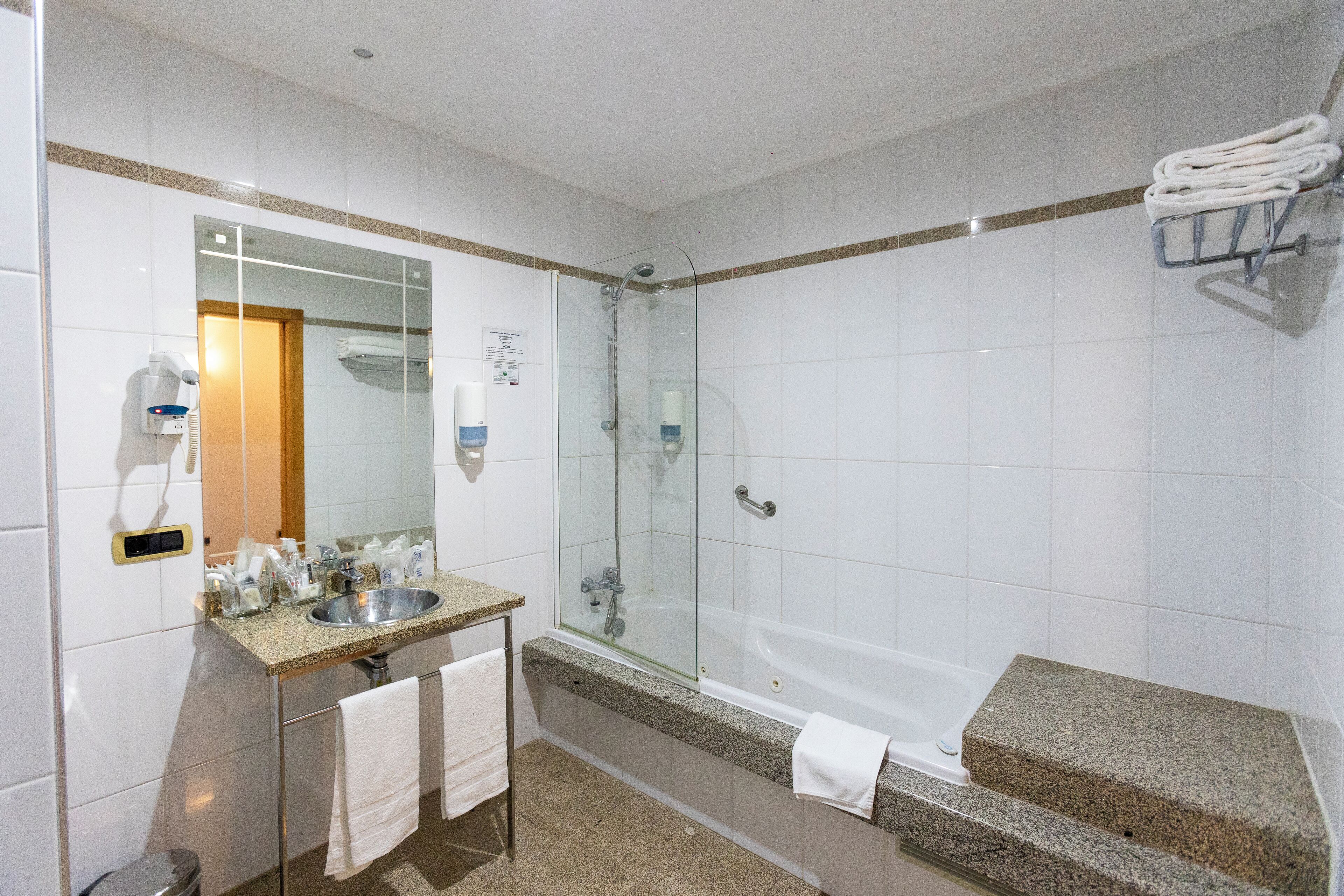 Un baño moderno con ducha de vidrio, lavamanos sobre encimera de granito y bañera independiente.