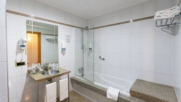 Un baño moderno con ducha de vidrio, lavamanos sobre encimera de granito y bañera independiente.