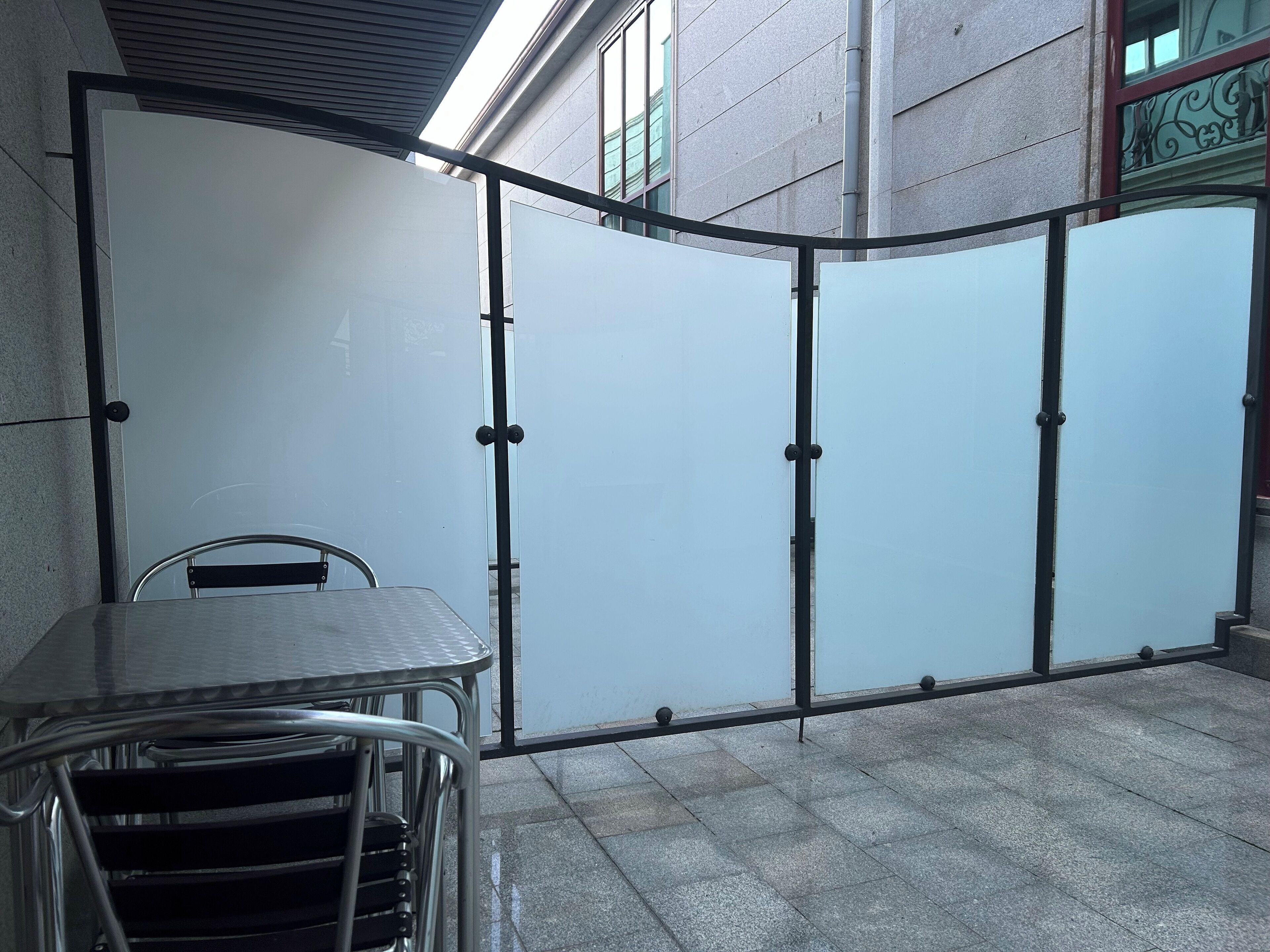 Een glazen scheidingswand met metalen frame, met een tafel en stoelen aan één kant.