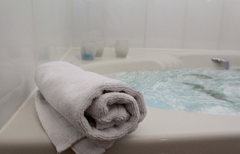 Un asciugamano bianco arrotolato su una vasca da bagno con l'acqua che scorre.