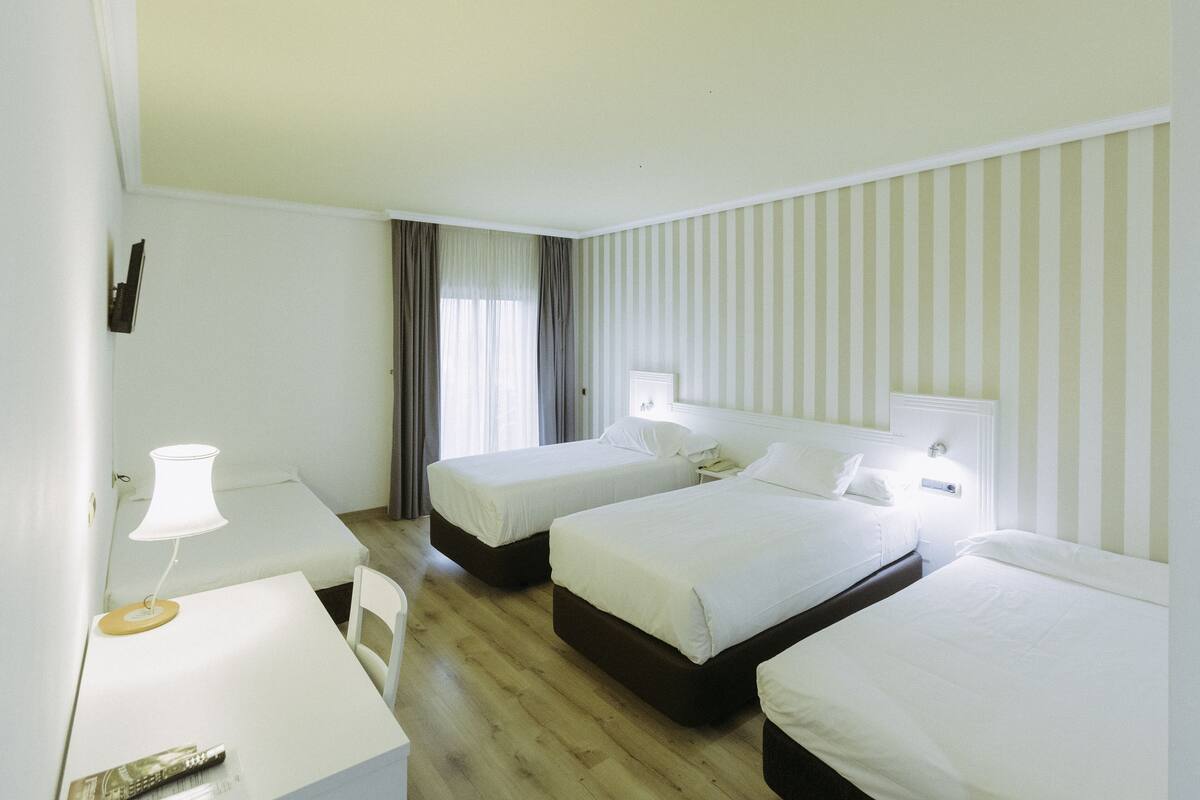 Habitación de hotel con dos camas individuales, un escritorio con lámpara y una silla.
