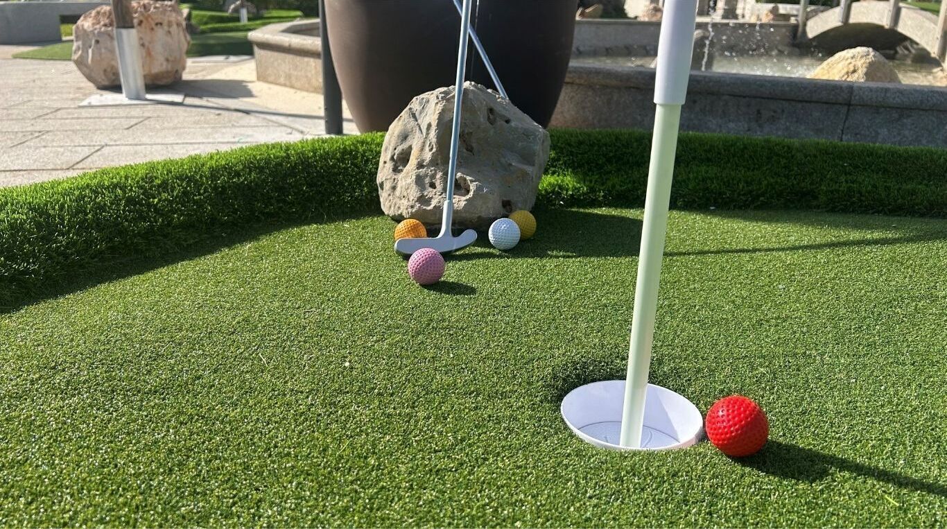 Un parcours de minigolf avec un gazon artificiel vert, un trou de golf blanc et des balles de golf colorées.