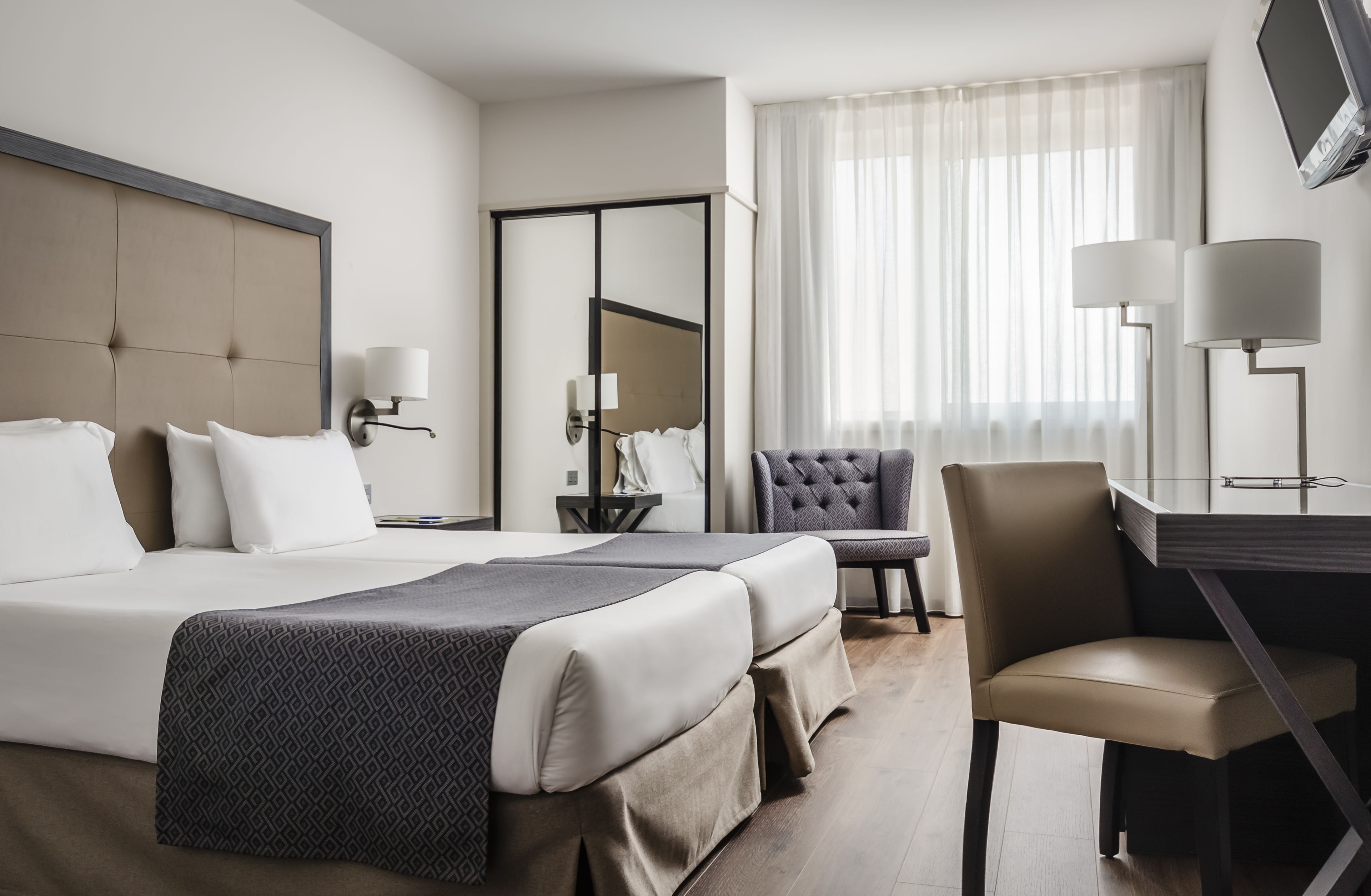 Una habitación de hotel con una cama grande, un escritorio con una silla, un espejo y un televisor.