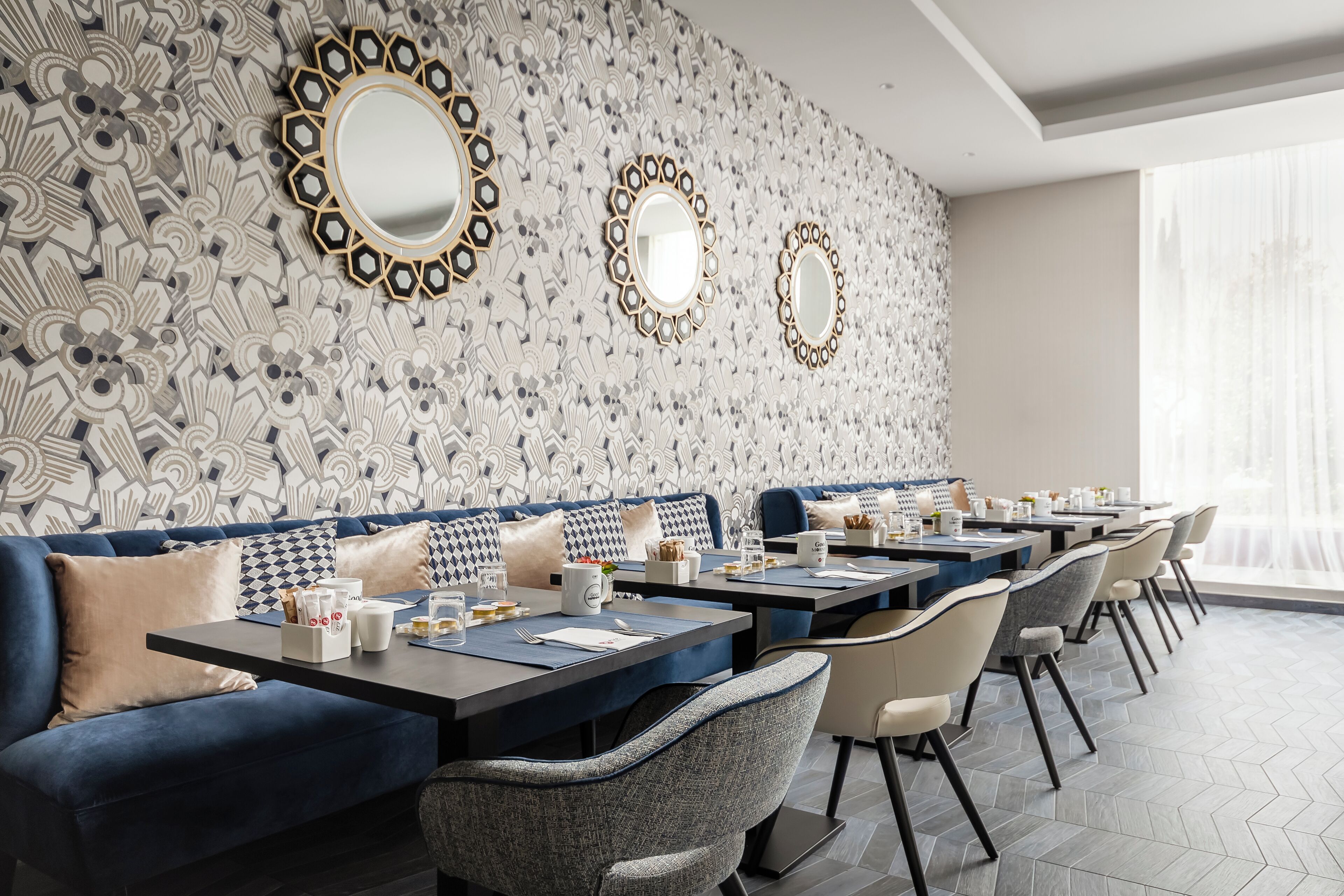 Un comedor moderno con pared decorativa, asientos azules y varias mesas.