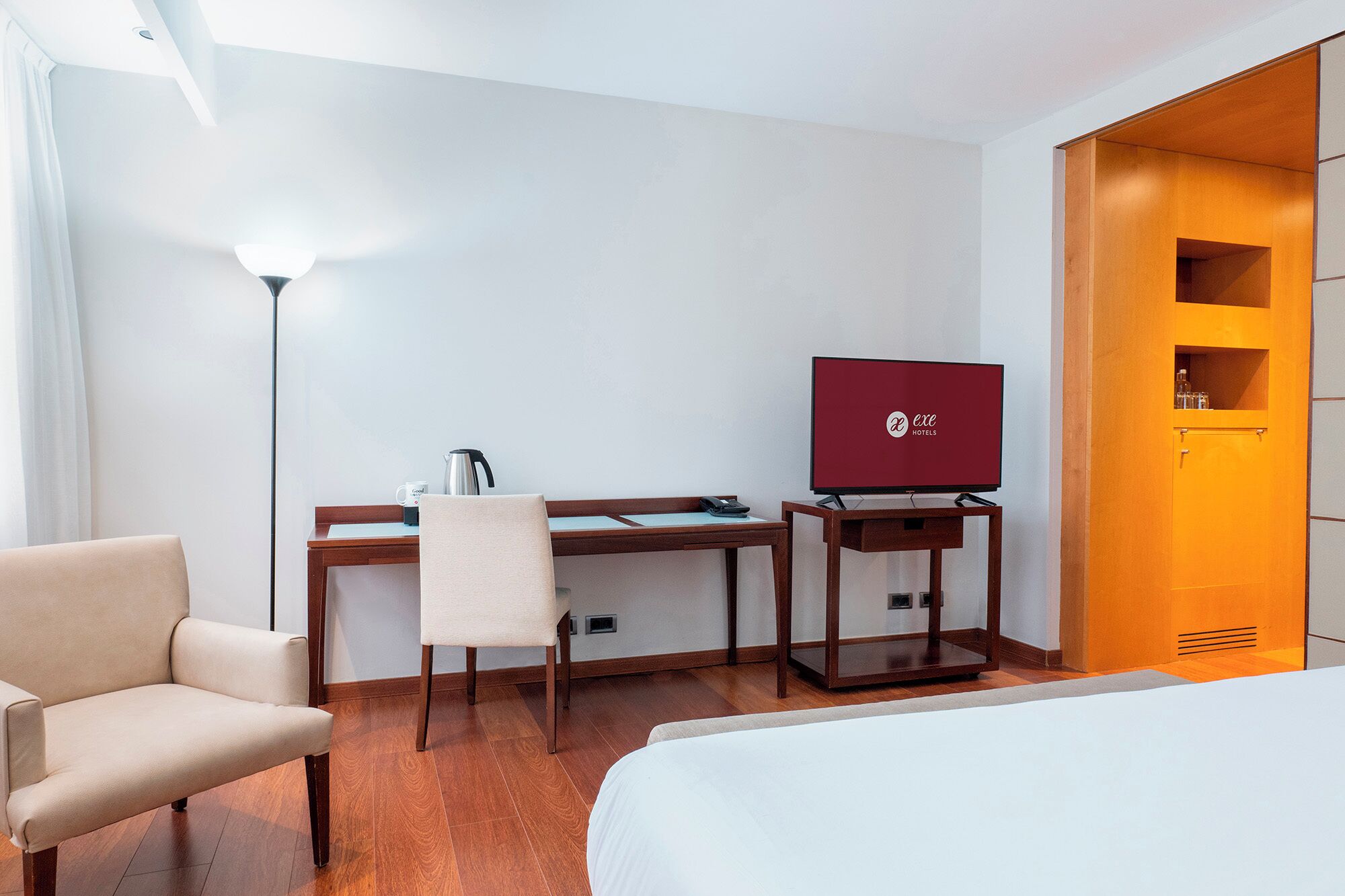 Una habitación de hotel con una cama, un escritorio con una silla, un televisor y un armario.