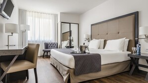 Une chambre d’hôtel comprenant un lit, une table de chevet, une lampe, une chaise et un bureau avec une autre chaise.
