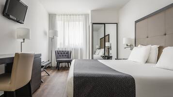 A hotel room with a bed, a desk, a chair, a TV, and a window with curtains.