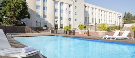 Un hotel con piscina, sillas de descanso y un cielo azul despejado.