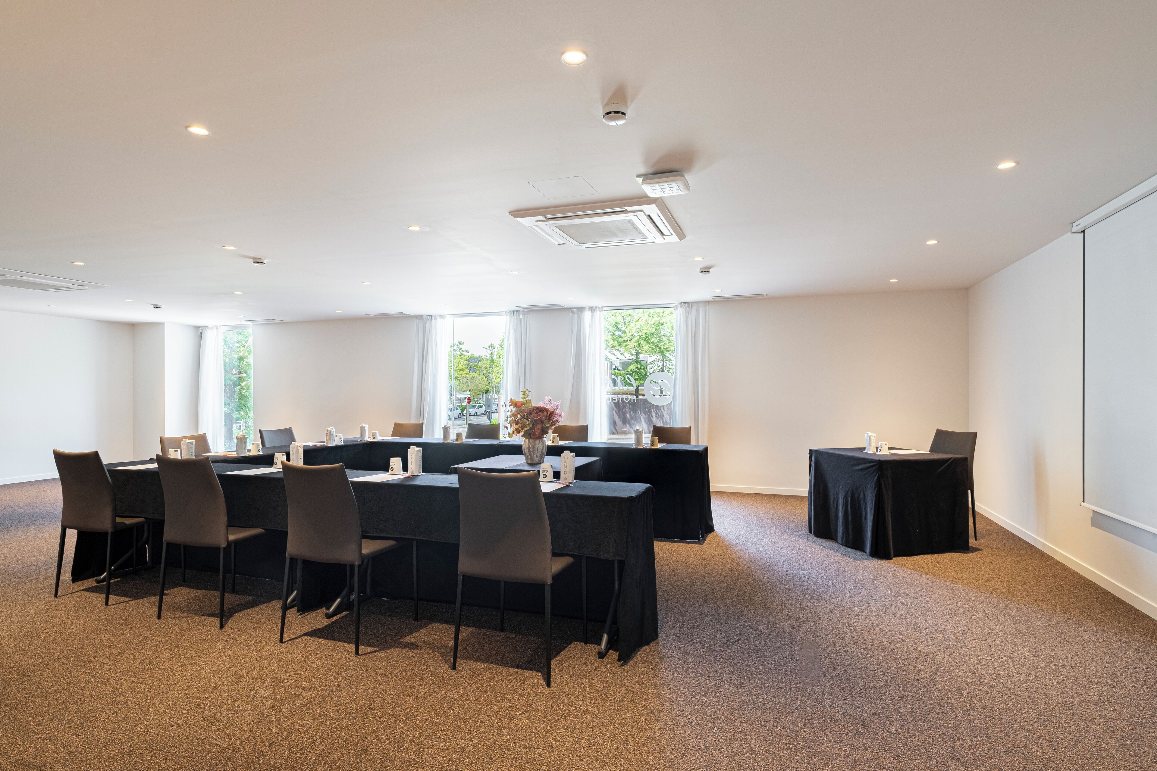 Une salle de conférence équipée d’une longue table, de chaises, d’un écran de projection et d’une grande fenêtre donnant sur un paysage verdoyant.