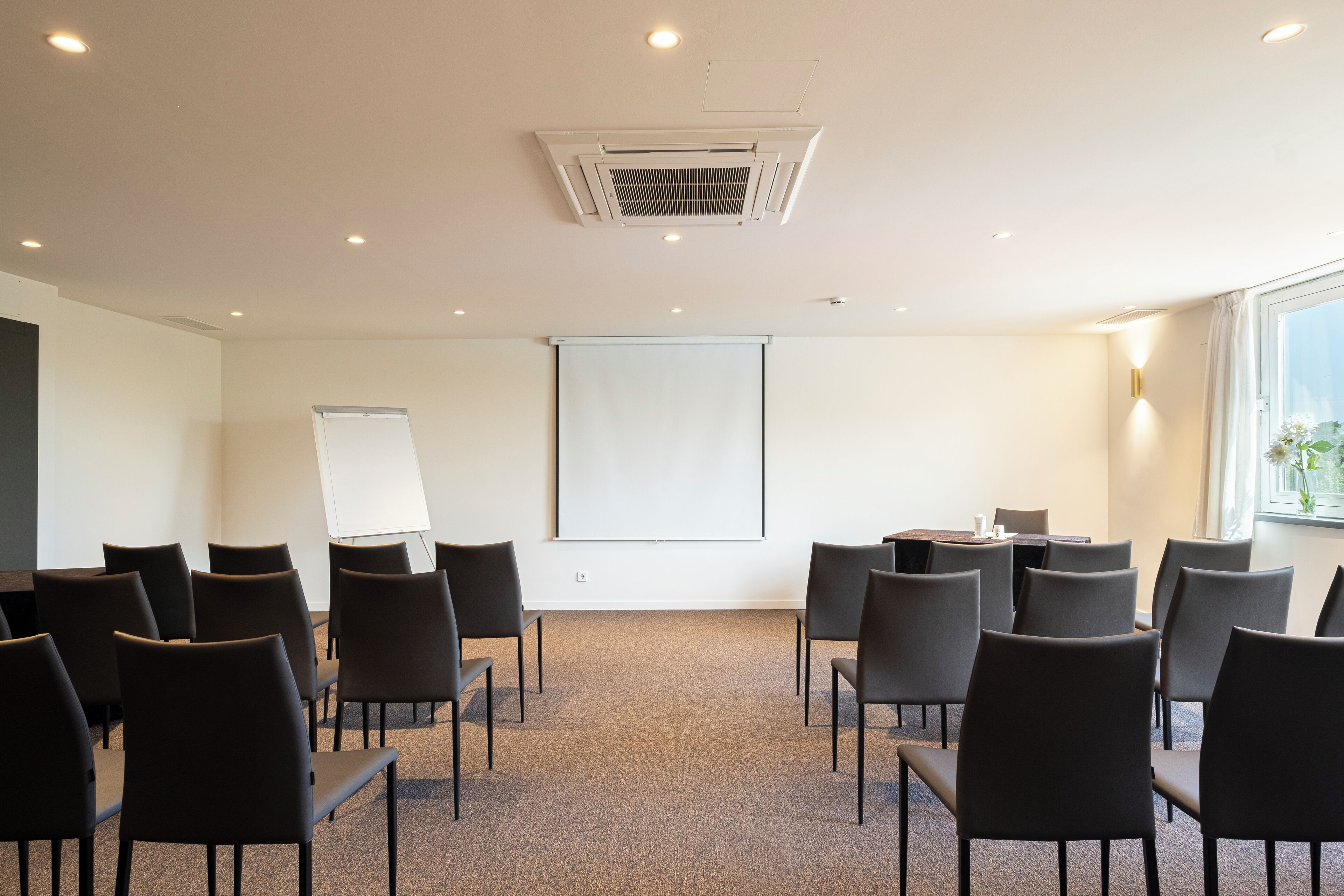 A conference room with a projector screen, a whiteboard, and several chairs arranged for a meeting.