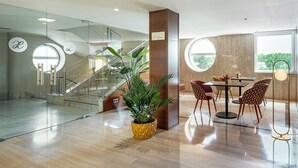 Un hall d’hôtel moderne avec un escalier, un espace repas avec des chaises et une grande plante en pot.