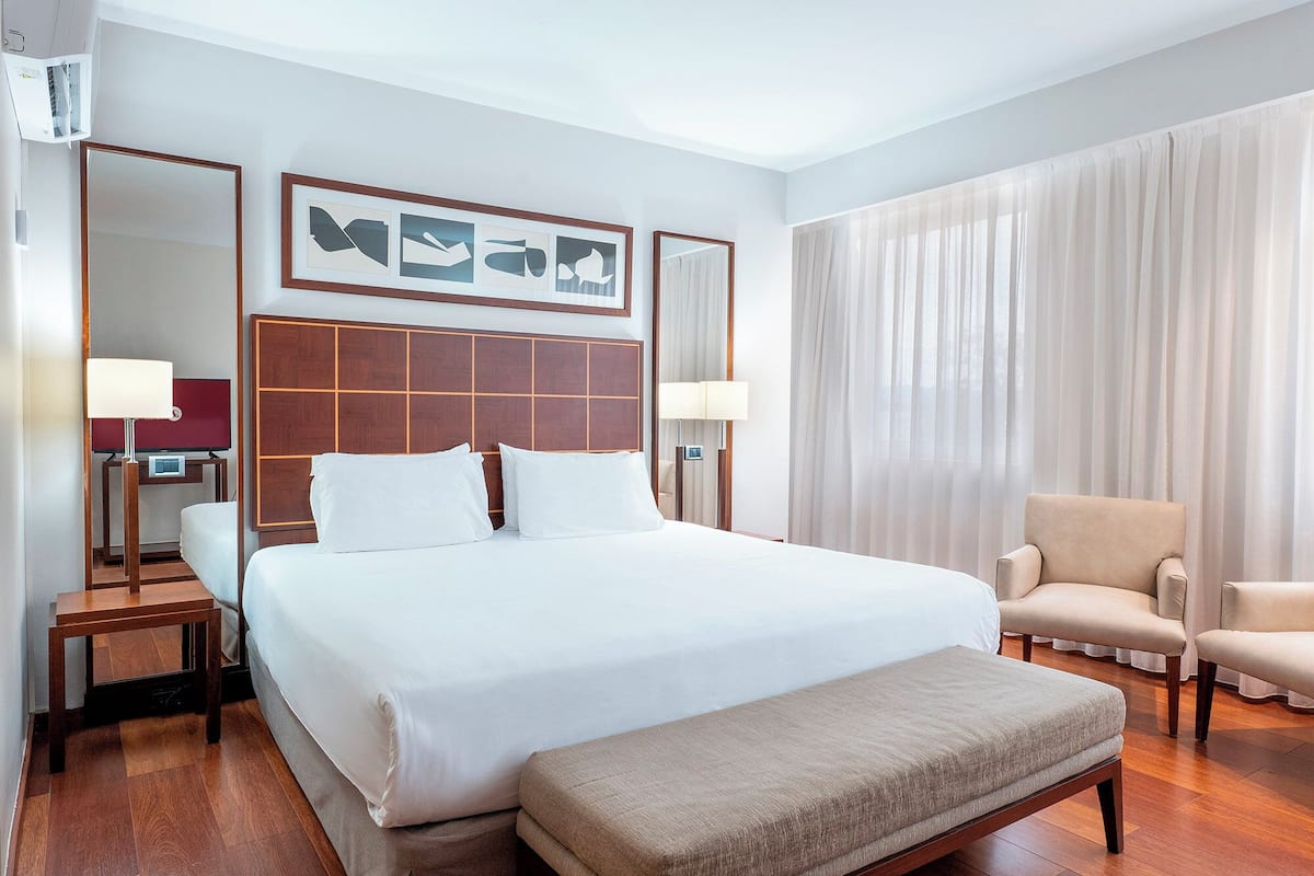 Una habitación de hotel con una cama grande, una mesita de noche, una silla, un televisor y un espejo.
