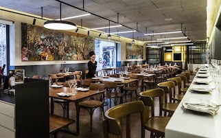Un restaurant avec de longues tables et des chaises en bois, et une fresque murale.