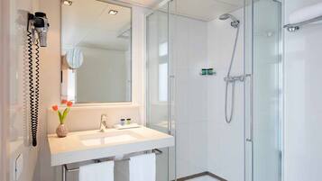 Een moderne badkamer met een glazen douchecabine, een grote spiegel en een witte wastafel met een bloevas.