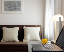 A modern living room with a brown sofa, two white pillows, a laptop, and a yellow rose on the table.
