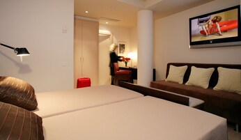 A hotel room with a bed, a sofa, a TV, and a desk with a chair.