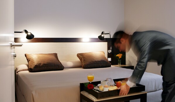 A neatly made bed with two pillows, a bedside table with a tray of breakfast items, and a nightstand with a vase of flowers.