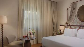 A hotel room with a bed, a chair, a small table with a vase of flowers, and a nightstand with a lamp.