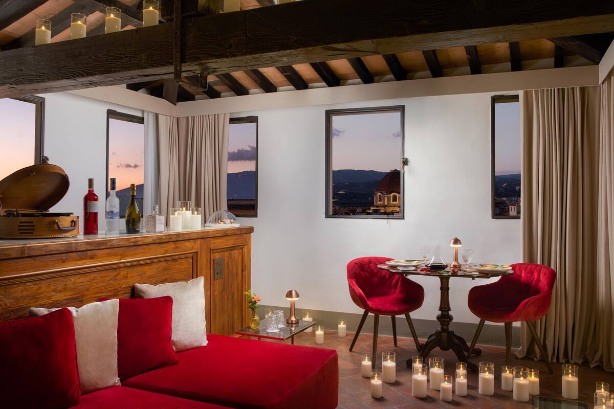 Une pièce avec un plafond en bois, un canapé rouge, une table à manger avec des chaises rouges, des bougies et une vue sur le paysage urbain à travers de grandes fenêtres.