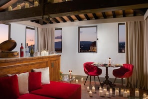 A room with a wooden ceiling, a red sofa, a dining table with red chairs, candles, and a view of a cityscape through large windows. - Porta Rossa Hotel Firenze Colbert Collection (Florence)