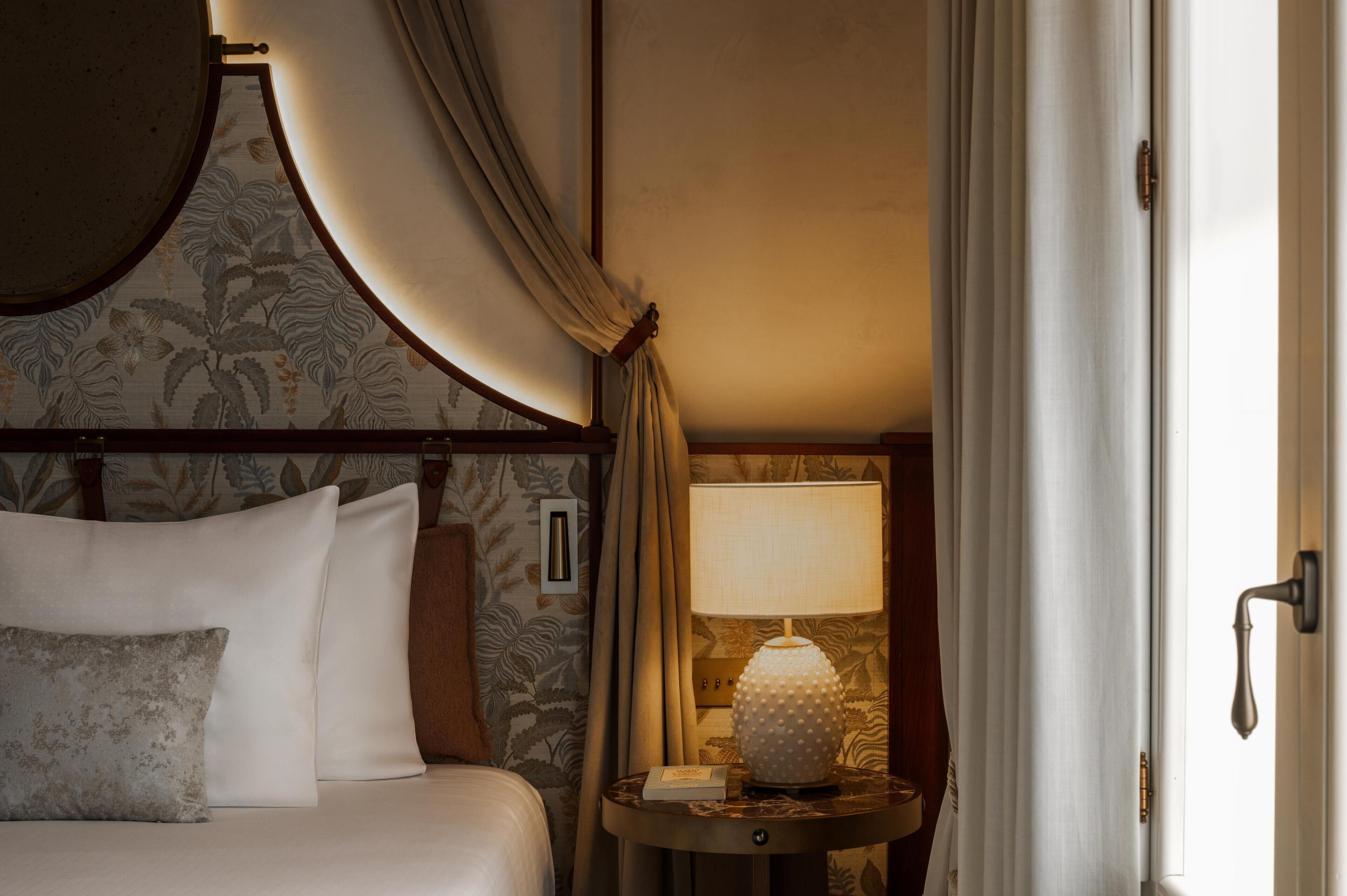 A hotel room with a bed, a nightstand with a lamp, and a door.