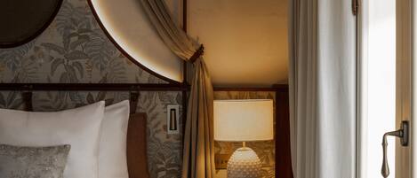 A hotel room with a bed, a nightstand with a lamp, and a door.