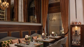 A hotel room with a checkered floor, a sofa with patterned cushions, a dining table with chairs, and a bar area with bottles. - Porta Rossa Hotel Firenze Colbert Collection (Florence)