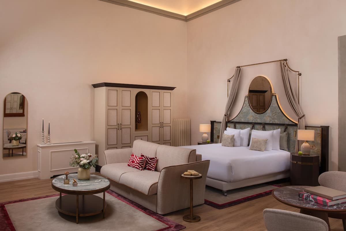 Une chambre d’hôtel comprenant un lit, un canapé, une table basse ronde, une table d’appoint, un miroir et un meuble de rangement.
