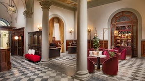 A lobby with checkered flooring, a reception desk, a red sofa, and a chandelier. - Porta Rossa Hotel Firenze Colbert Collection (Florence)