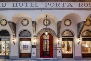 Facciata di un hotel con finestre ad arco, ingresso centrale con tappeto rosso e insegna sopra l'ingresso.